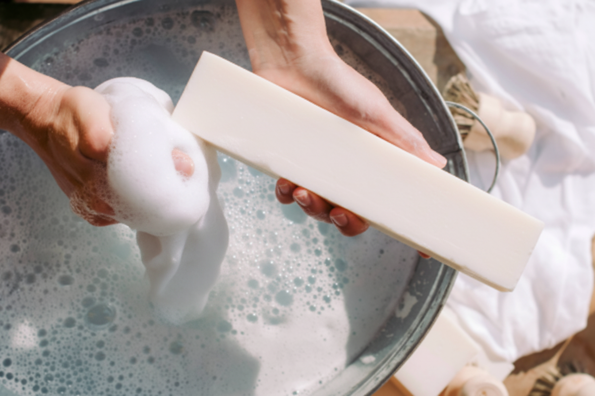 Hands washing white laundry with the Pure Tallow laundry soap bar over a basin of soapy water