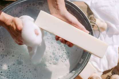 Hands washing white laundry with the Pure Tallow laundry soap bar over a basin of soapy water